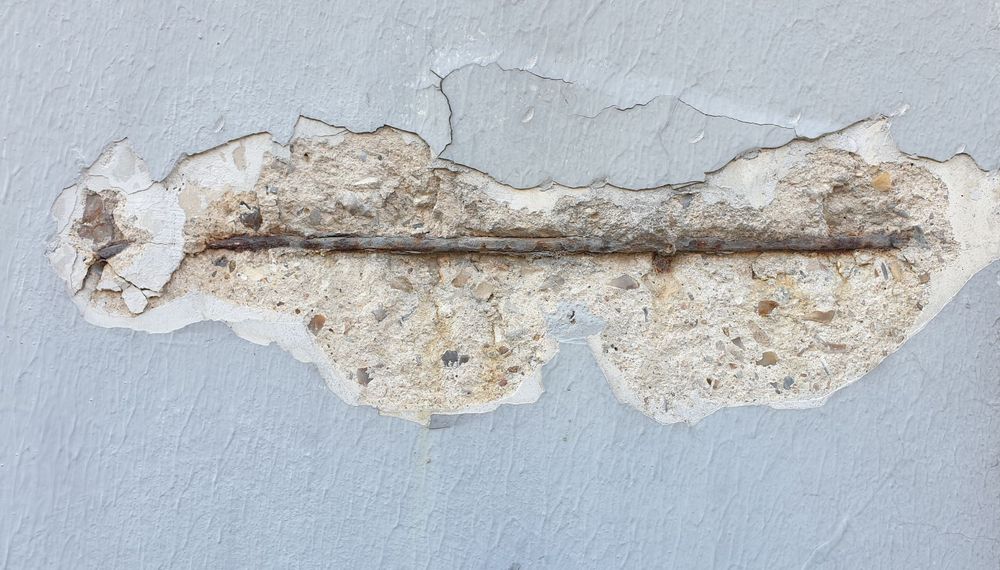 Dettaglio di calcestruzzo degradato con fessure e armature esposte, simbolo di deterioramento strutturale.